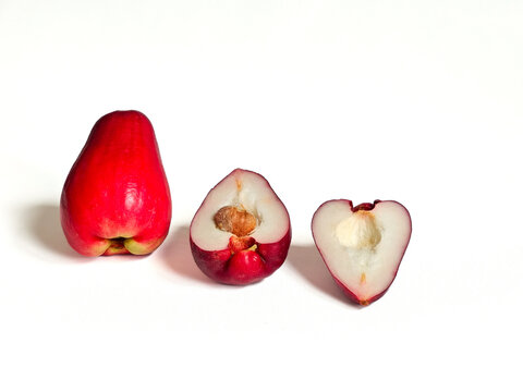 Fresh wax apple (Syzygium samarangense) fruit standing on white surface with visible base, beside two halved pieces showing inner flesh and single seed, isolated on white background