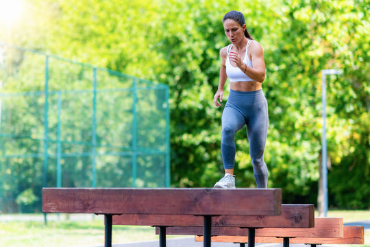 Athletic woman stepping on wooden obstacle, performing balance and coordination exercise in outdoor park gym.