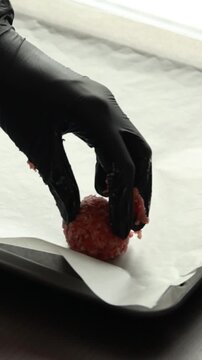 Vertical close-up of hands arranging raw turkey meatballs in neat rows on a baking tray ready for the oven