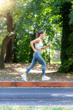 Woman running along wooden beam in park, performing agility and balance exercise as part of functional fitness training.