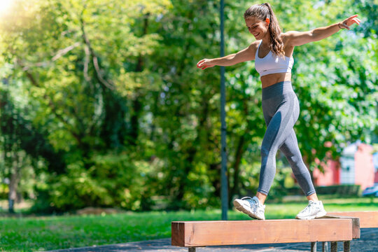 Athletic woman stepping forward on narrow beam, focusing on balance, coordination and functional outdoor fitness training.