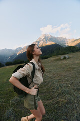 Naklejka premium Active woman hiking outdoors with backpack in alpine meadow, mountains in the background. Adventure, nature, wellness, and outdoor lifestyle for motivation and balance.