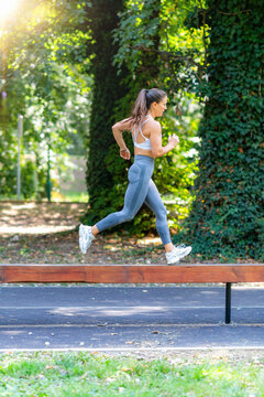Athletic woman sprinting on narrow wooden beam, combining balance, coordination and speed in outdoor workout session.
