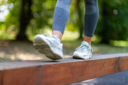 Close-up of woman stepping forward on wooden beam, focusing on balance, coordination and controlled movement.
