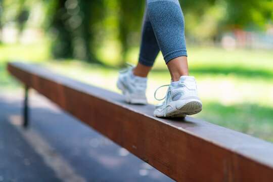 Rear view of athletic woman walking along narrow beam, performing balance and stability training in park environment.