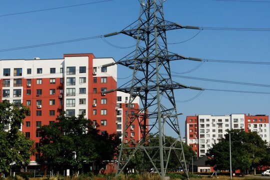 Metal tower with high voltage wires crosses path of modern residential buildings. Urban infrastructure connects city life with power supply grid.