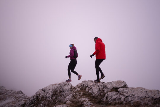 Couple Hiking on Foggy Mountain Ridge in Winter Jackets During Outdoor Adventure and Trail Run