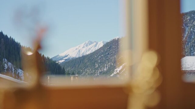 Beautiful snowy mountain peaks and pine forest view from a warm and cozy wooden chalet window