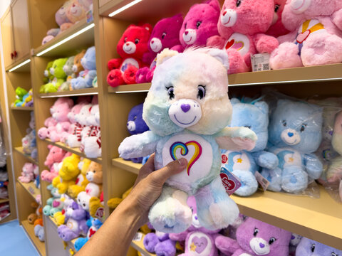 KUALA LUMPUR, MALAYSIA - FEB 02, 2026: Close up of a hand holding pastel Care Bears plush toy in retail store with colorful stuffed animal shelf background.
