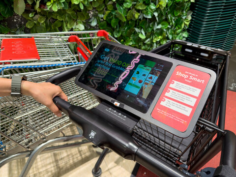 KUALA LUMPUR, MALAYSIA - FEB 02, 2026: Close up of a smart shopping cart touchscreen display in supermarket retail store with hand on handlebar.