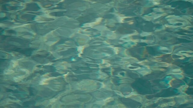 Close-up of turquoise pool water shimmering in soft dry light, reflecting sunlight with gentle ripples. Minimal, calming abstract texture ideal for backgrounds and summer themes.