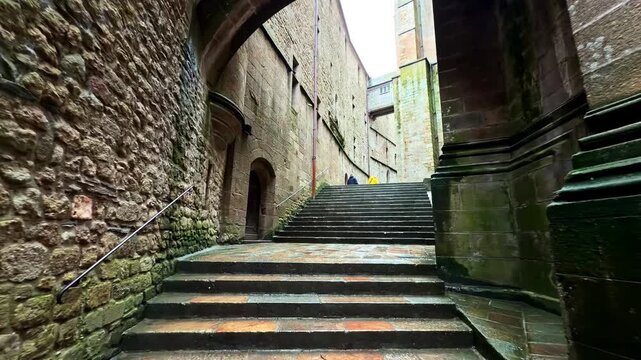 A quiet stone passageway leads through Mont-Saint-Michel with moss-covered walls. Ideal for historical or architectural content.