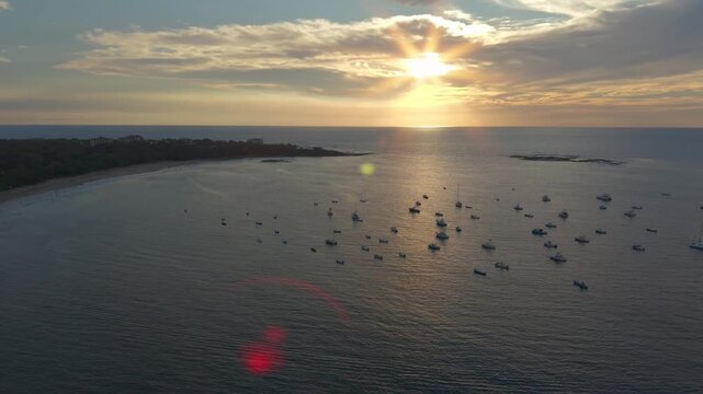 Aerial pan right over Tamarindo bay at sunset with golden light reflecting on ocean and anchored boats.