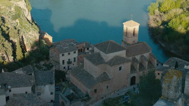 An elevated view over Miravet, Spain, shows church rooftops above the Ebro River, combining medieval architecture, calm water, and strong historic village character.