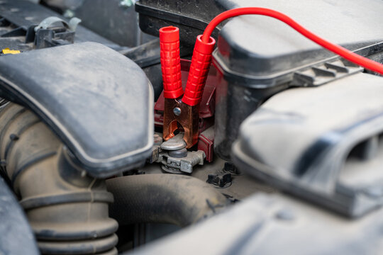 a red jumper cable clamp being attached to the positive terminal of a car battery to jump-start a vehicle.