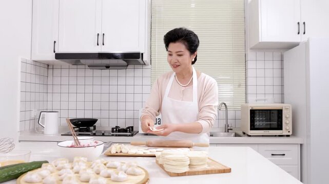 Portrait elderly woman chef wear apron rolls out dough with hands for making tasty homemade dumplings stuffed with minced meat vegetable, wrapped dough on table. Concept of home cooking. Family recipe