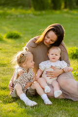 Fototapeta premium mother with two daughters sitting on a lawn at sunset in the summer, hugging