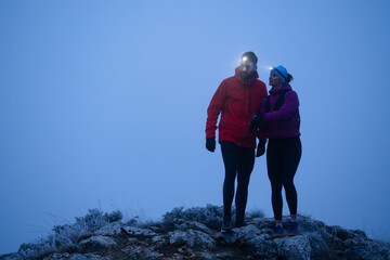 Fototapeta premium Couple Hiking With Headlamps On Foggy Mountain Summit During Twilight Winter Outdoor Adventure