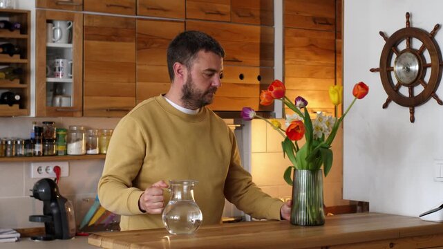 Caring man arranging flowers in a vase at home