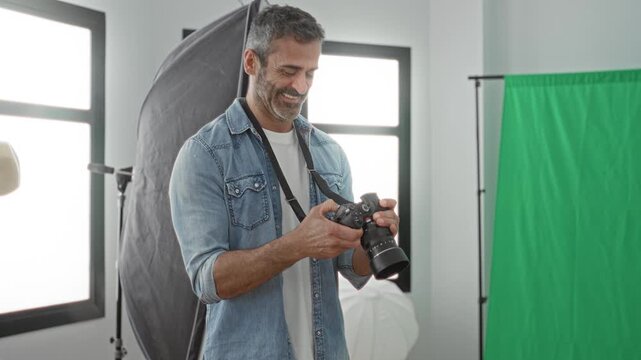 Man holding camera checks settings and smiles while adjusting lens and reviewing image preview on dslr in studio; focused.