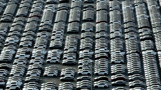 Drone aerial view of modern cars arranged in perfect rows at an advanced vehicle production facility, symbolizing automation, autonomous driving technology, and the future of sustainable mobility. 4k.
