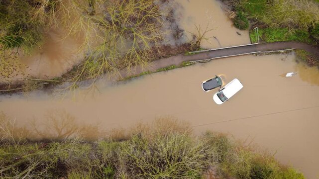 Flooded cars after hurricane rainfall covering rural road with muddy water. Extreme storm flooding submerging vehicles and surrounding countryside landscape. Natural disaster causing severe damage and