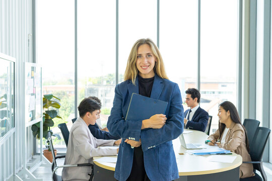 Smiling female executive looking at camera, happy businesswoman posing with office people at background.