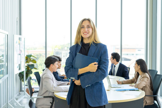 Smiling female executive looking at camera, happy businesswoman posing with office people at background.