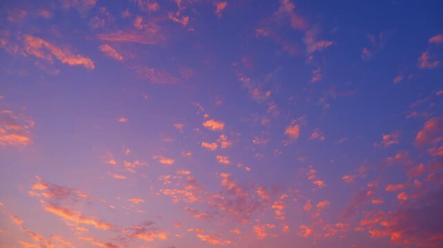 A sunset sky timelapse video footage with glowing altocumulus clouds scattered across a deep blue twilight sky, featuring warm orange highlights, dynamic cloud motion, serene evening atmosphere. 4k.
