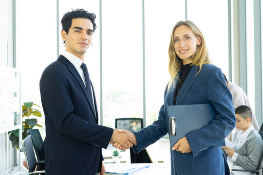 Businesswoman and businessman leader looking at camera in modern office with businesspeople working at the background. Teamwork concept. 