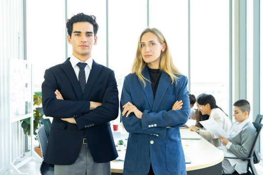 Businesswoman and businessman leader looking at camera in modern office with businesspeople working at the background. Teamwork concept. 