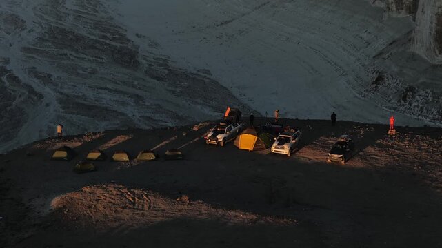 Aerial view of a campsite with tents and off-road vehicles on a cliff edge at sunrise in Bozjyra Aktau, Mangystau Region, Kazakhstan.