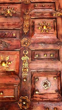 Vertical tilt down shot of an ancient, ornate wooden door featuring decorative brass studs and traditional Islamic patterns