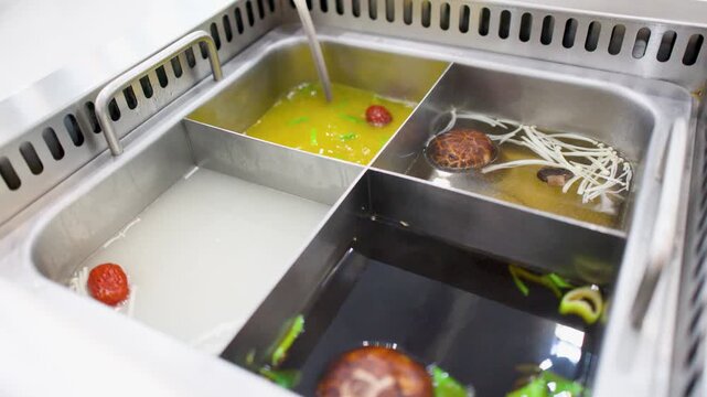 Ladle Stirring Mushroom Broth in a Four Section Chinese Hot Pot
