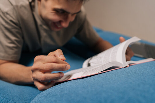 Cheerful man engrossed in reading a book, leisure activity on comfortable blue couch at home, focusing on education, knowledge, and personal growth, finding joy and peace in literature.
