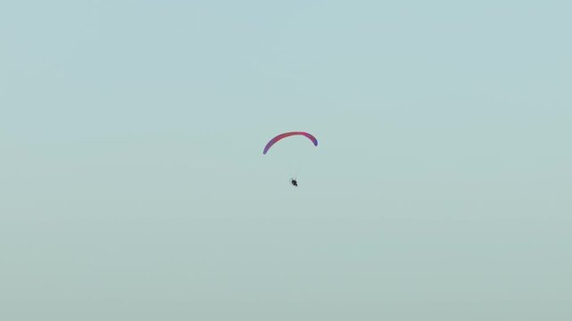 Powered paraglider canopy arcing across clean sky while paramotor pilot cruising through open atmosphere. Paramotoring activity continuing steady aerial navigation extreme adventure sport lifestyle