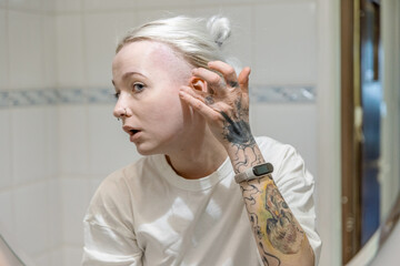 Fototapeta premium A young woman with piercings and tattoos checking her hair looking at mirror