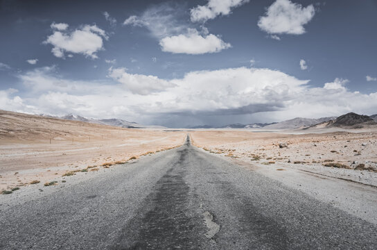 The Pamir Highway in the Tien Shan highlands of the Pamirs in Tajikistan, an asphalt road stretching into the distance, desert terrain with mountains