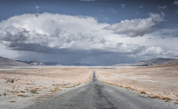 The Pamir Highway in the Tien Shan highlands of the Pamirs in Tajikistan, an asphalt road stretching into the distance, desert terrain with mountains