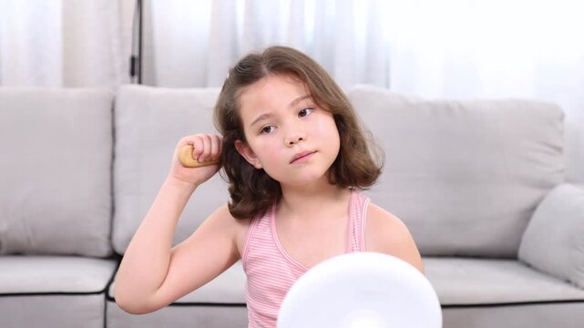 Happy young adorable girl with playful smile styles her hair with curlers while sitting at dressing table, embracing self-care and personal grooming, styling herself in front of a mirror at home.