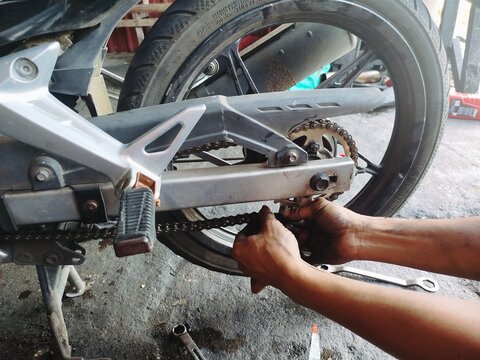 KUALA TERENGGANU MALAYSIA- MAY 07. 2026..  "Close-up of motorcycle rear wheel and chain assembly during maintenance. Hands tighten chain with wrench in a garage workshop setting."