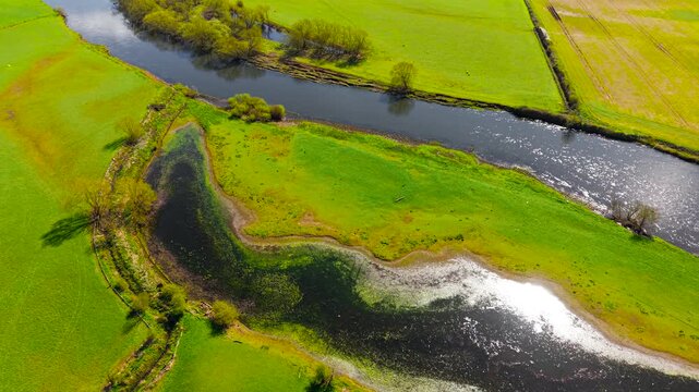 Detailed aerial view oxbow lake near river with muddy shoreline and shallow water textures in farmland. Close drone perspective vegetation patterns water clarity and seasonal landscape changes