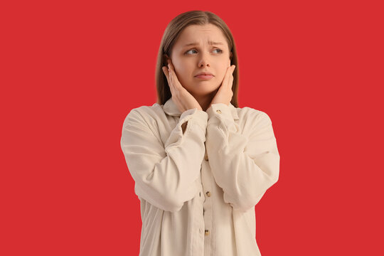 Young woman suffering from loud noise on red background