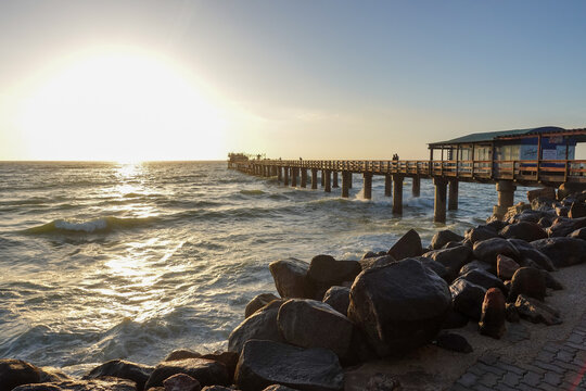 As the sun sinks beyond the Atlantic, the waterfront of Swakopmund&nbsp;glows in warm light, where ocean mist, silhouettes, and evening colors merge into a calm coastal scene.