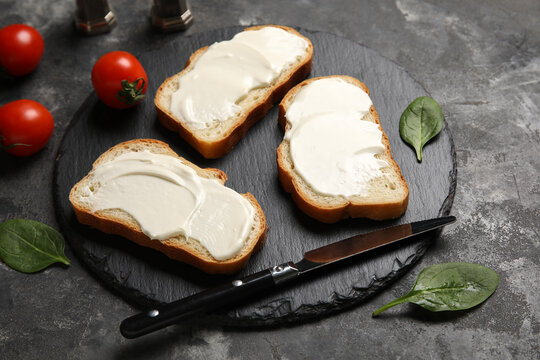 Black slate board of tasty bruschetta with processed cheese, spinach leaves and fresh tomatoes on black background. Closeup
