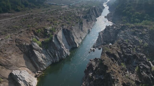 Bhedaghat's Narmada River cuts through towering marble rock cliffs in Jabalpur District, Madhya Pradesh. Smooth aerial tracking shot follows the river upstream through the narrow limestone canyon.