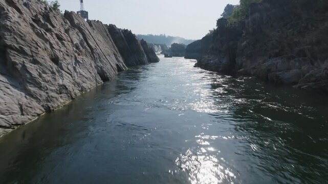 Narmada River flows through narrow marble rock canyon toward Dhuandhar Falls at Bhedaghat near Jabalpur. Smooth forward tracking shot follows the water through towering geological formations.