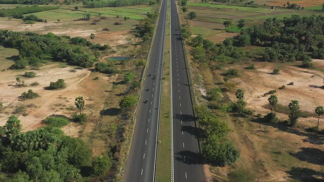 Tamil Nadu's Grand Trunk Road cuts through patchwork agricultural fields with scattered palm trees and sparse traffic. Aerial forward tracking shot maintains centered framing over the divided highway.
