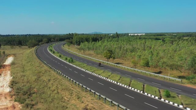 Grand Trunk Road curves through rural Tamil Nadu landscape with agricultural fields and tree plantations. Aerial view captures divided highway with white lane markings and safety barriers.