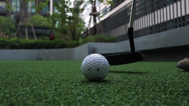 Close up of golf ball and putter on artificial green surface.